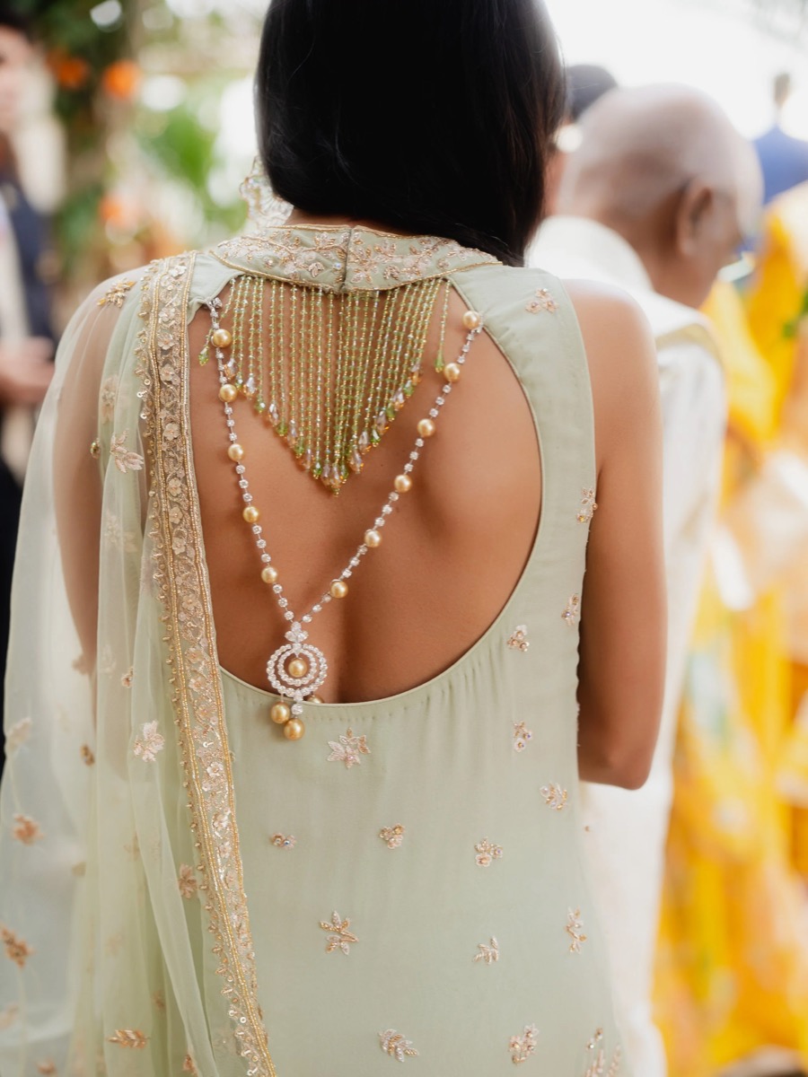 Woman wearing a green dress with embroidery and layered pearl and gemstone jewelry, at a cultural or celebration event.