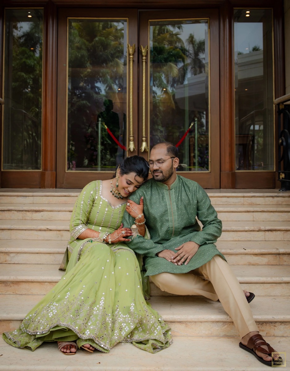 A couple in traditional Indian attire sitting on steps outside a building, sharing a tender moment.