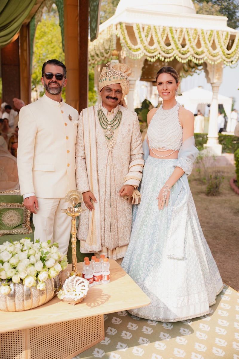 Three people dressed in traditional and wedding attire standing together beneath a decorated canopy at a wedding ceremony.