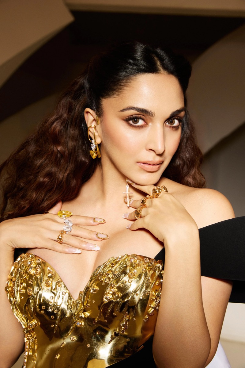 A woman with wavy brown hair wearing gold jewelry and a gold and black dress.