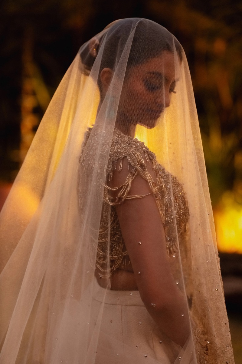 A woman in a wedding dress with a veil, standing outdoors at sunset or during dusk.