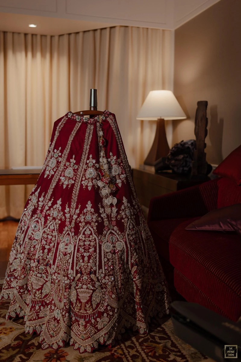 An ornately embroidered red and gold skirt draped over a mannequin, inside a warmly lit room with curtains, a lamp, and a sofa.